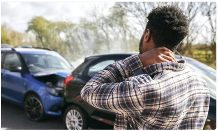 Young man rubbing neck in pain from whiplash injury standing by damaged car after traffic accident