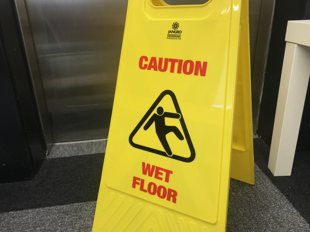 A yellow "Caution Wet Floor" sign over wet floor tiles.