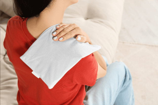 Woman using a heating pad on her shoulder as part of her injury treatment.