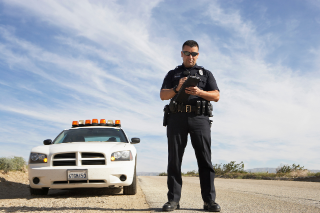 Police officer standing in front of police car filling out a report.