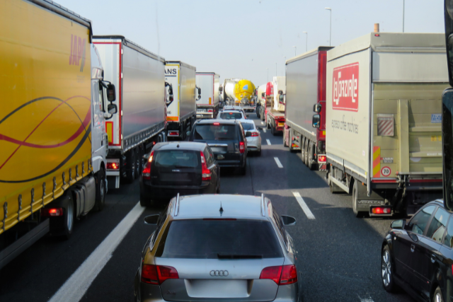 Line of smaller cars driving between trailer trucks on both sides of the road.